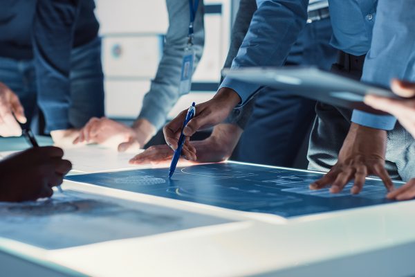 Engineer, Scientists and Developers Gathered Around Illuminated Conference Table in Technology Research Center, Talking, Finding Solution and Analysing Industrial Engine Design. Close-up Hands Shot